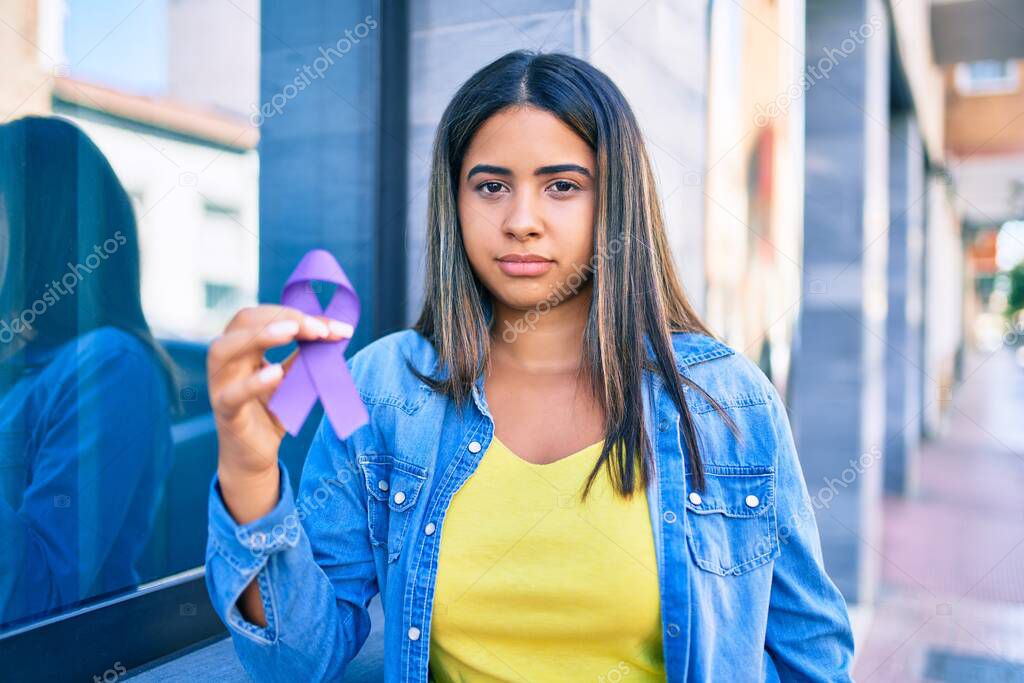 Young latin woman with serious expression holding purple ribbon at city.