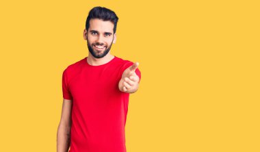 Sakallı, sıradan tişörtler giyen, dostça gülümseyerek selamlaşan genç yakışıklı bir adam. başarılı iş. 