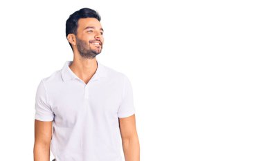 Genç, yakışıklı, günlük kıyafetler giyen, yüzünde gülümseme ve doğal bir ifadeyle yan yana bakan İspanyol bir adam. Kendinden emin gülen. 