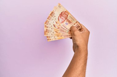 İspanyol eli 100 Meksika pezosu tutuyor. İzole edilmiş pembe arka planda..