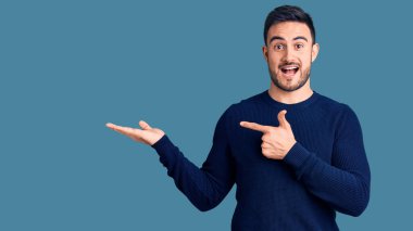 Gündelik kıyafetler giyen genç yakışıklı adam kameraya hayret ediyor ve gülümsüyor.. 