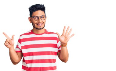 Yakışıklı Latin Amerikalı gündelik kıyafetler ve gözlük takan genç adam yedinci parmaklarını gösterip gösterirken kendinden emin ve mutlu gülümsüyor.. 