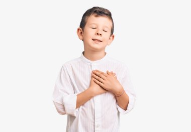 Zarif tişört giyen, göğsünde elleri kapalı, yüzünde minnet dolu bir jest olan sevimli sarışın çocuk. sağlık kavramı. 