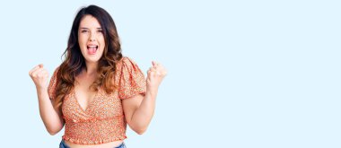 Güzel, genç, esmer bir kadın gündelik giysiler giyip kollarını kaldırıp, gözleri açık bir şekilde başarıyı kutluyor. Kazanan konsept. 