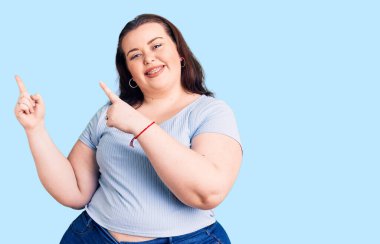 Gündelik kıyafetler giyen, gülümseyen ve kameraya bakan, iki eli ve parmağı yanda olan genç bir kadın.. 