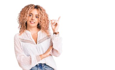 Kıvırcık saçlı, zarif bir yaz gömleği giyen, yüzünde kocaman bir gülümseme olan, eli ve parmağı kameraya bakan genç sarışın kadın.. 