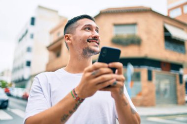Şehrin caddesinde akıllı telefon kullanan, mutlu gülümseyen genç İspanyol adam..