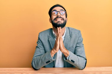 Ofiste çalışan genç İspanyol bir adam elleri bağlı yalvarıyor ve dua ediyor. Yüzünde umut ifadesi var. Çok duygusal ve endişeli. Yalvarıyor. 