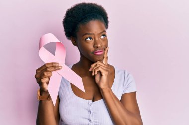 Genç Afro-Amerikalı kız pembe kanser kurdelesi takmış ciddi bir yüz ifadesiyle eli çenesinde soruyu düşünüyor, kafa karıştırıcı bir fikir. 