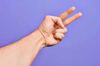 İzole edilmiş mor arka planda parmaklarını gösteren beyaz bir gencin eli iki parmağı gösteriyor, işaret ediyor zafer ve kazanan sembol.