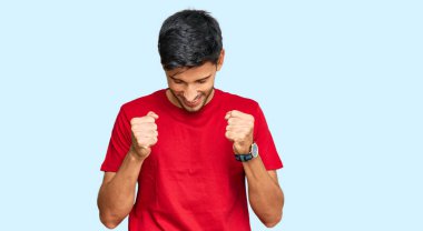 Başarı için heyecanlı kırmızı tişört giyen genç yakışıklı adam kollarını kaldırmış ve gözleri kapalı zaferi kutluyor. Kazanan konsept. 