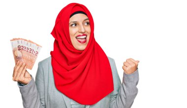 İslamcı başörtüsü takan güzel İspanyol kadın elinde 10 avroluk banknotlarla baş parmağını kaldırıyor ve ağzı açık gülümsüyor. 