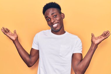 Genç Afro-Amerikan adam günlük kıyafetler giyiyor gülümseyerek iki elini de açık tutuyor, sunuyor ve reklam karşılaştırması yapıyor ve dengeyi sağlıyor. 