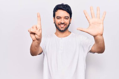 Latin asıllı genç adam gündelik giysiler giyip altı numaralı parmaklarıyla işaret ederken kendinden emin ve mutlu bir şekilde gülümsüyor.. 