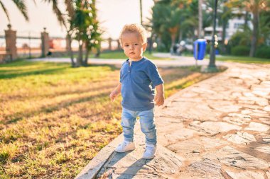 Sevimli ve mutlu küçük çocuk güneşli bir günde parkta eğleniyor. Güzel sarı saçlı erkek çocuk dışarıda oynuyor.