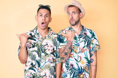 Yaz şapkası ve Hawaii tişörtü giyen iki genç eşcinsel, elleri yana dönük, ağzı açık, şaşkın bir ifadeyle şaşırdılar.. 