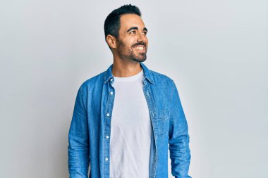 Latin kökenli genç bir adam günlük giysiler giyiyor, rahat bir görünüm takınıyor, doğal bir yüz ifadesi ve kendinden emin bir gülümsemeyle poz veriyor.. 