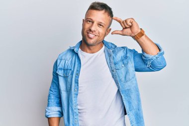 Yakışıklı, sıradan bir kot ceket giyen, gülümseyen, kendine güvenen, el hareketi yapan, parmaklarıyla işaret eden ve kameraya bakan kaslı bir adam. ölçüm kavramı. 