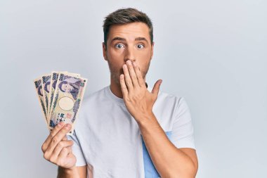 Elinde 5000 japon doları tutan yakışıklı beyaz adam ağzını eliyle kapatıyor, şaşırmış ve hata yapmaktan korkuyor. şaşırmış ifade 