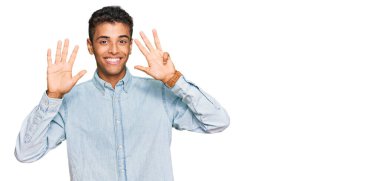 Genç, yakışıklı, Afro-Amerikalı, günlük kıyafetler giymiş, dokuz numaralı parmaklarıyla gösteriş yapan, kendinden emin ve mutlu bir şekilde gülümseyen.. 