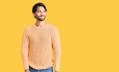 Yakışıklı İspanyol bir adam, sıradan bir süveter giyiyor, gülümsüyor, yan tarafa bakıyor ve düşünüyor.. 