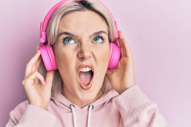 Kulaklıkla müzik dinleyen genç sarışın kız kızgın ve kızgın çığlıklar atıyor öfkeyle bağırıyor, öfkeyle yukarı bakıyor.. 