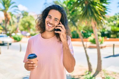 Genç İspanyol adam gülümsüyor. Akıllı telefonla konuşuyor ve şehirde kahve içiyor..