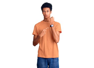 Genç, Afro-Amerikalı, günlük giysiler içinde. Saati, sabırsızlığı ve rahat bir ifadeyle kameraya bakması için acele ediyor. 