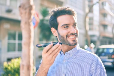 Genç İspanyol adam gülümsüyor. Şehirdeki akıllı telefonu kullanarak sesli mesaj gönderiyor..