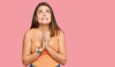 Kafkasyalı genç bir kadın gündelik giysiler giyip elleri bağlı yalvarıyor ve dua ediyor. Yüzünde umut ifadesi var. Çok duygusal ve endişeli. Yalvarıyor. 