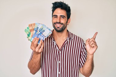 Sakallı yakışıklı İspanyol adam Güney Afrika rand banknotları tutuyor mutlu bir şekilde gülümsüyor. 