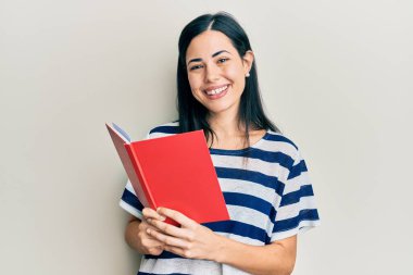 Güzel genç bir kadın kitap okuyor. Olumlu ve mutlu görünüyor. Kendine güvenen bir gülümsemeyle ayakta duruyor ve dişlerini gösteriyor. 