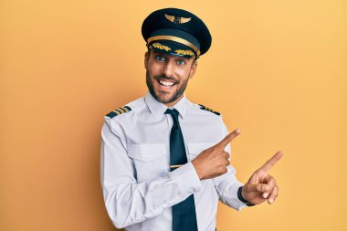 Yakışıklı, İspanyol pilot üniforması giyen, gülümseyen ve kameraya bakan iki eli ve parmakları yanda olan bir adam.. 