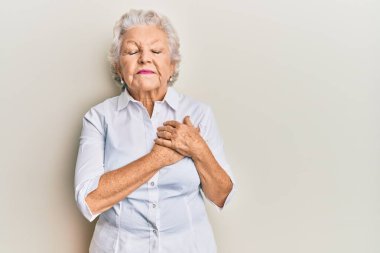 Yaşlı, gri saçlı, sıradan kıyafetler giyen, elleri göğsünde gülümseyen, gözleri kapalı, yüzünde minnet ifadesi olan bir kadın. sağlık kavramı. 