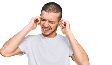 Gürültülü müzik sesi için günlük beyaz tişört giyen İspanyol genç adam kulaklarını parmaklarıyla kapatıyor. sağır kavramı. 