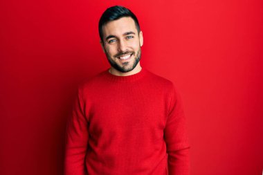 Yüzünde mutlu ve havalı bir gülümseme olan sıradan kıyafetler giyen genç İspanyol bir adam. şanslı kişi. 