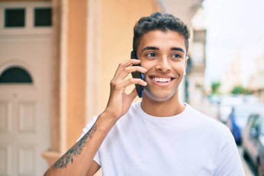 Genç Latin adam gülümsüyor ve şehirde akıllı telefondan konuşuyor..