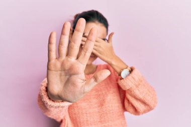 Gündelik kıyafetler ve gözlük takan genç, beyaz bir kadın ellerle gözlerini kapatıyor ve üzgün ve korku dolu bir ifadeyle dur hareketi yapıyor. utangaç ve olumsuz kavram. 