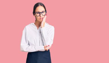 Güzel, esmer, profesyonel garson önlüğü giyen genç bir kadın kollarını kavuşturarak depresyondan sıkılmış ve yorgun görünüyor.. 