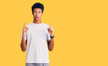 Gündelik giysiler giyen genç Afro-Amerikan adam şaşkın ve şaşırmış bir şekilde yukarı baktı ve parmaklarıyla işaret etti ve kollarını kaldırdı.. 