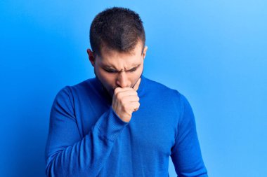 Gündelik kazak giyen genç yakışıklı adam kendini iyi hissetmiyor ve soğuk algınlığı veya bronşitin belirtisi olarak öksürüyor. sağlık hizmeti kavramı. 