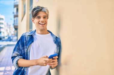 Genç İspanyol adam şehirde akıllı telefon kullanarak mutlu gülümsüyor..