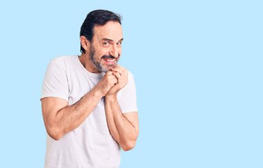 Orta yaşlı yakışıklı bir adam sıradan tişörtler giyiyor. Gergin ve heyecanlı bir şekilde çenesine bakıp yan tarafa bakıyor. 