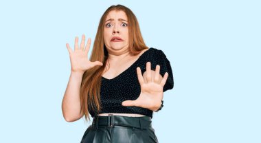 Zarif kıyafetler giyen, korku ifadesinden korkmuş ve dehşete düşmüş genç, güzel, kızıl saçlı bir kadın. El kol hareketi yapmayı kes, şok içinde bağır. panik konsepti. 