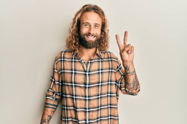 Sakallı, uzun saçlı, sıradan kıyafetler giyen, kameraya gülümseyen ve zafer işareti yapan yakışıklı bir adam. İki numara.. 