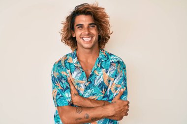 Yazlık tişört giyen, kollarını kavuşturup kameraya gülümseyen genç İspanyol adam. pozitif kişi. 