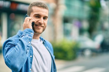 Genç beyaz adam gülümsüyor. Şehirdeki akıllı telefondan konuşuyor..