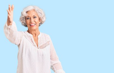 Son sınıftaki gri saçlı kadın, günlük kıyafetler giyip kameraya bakıyor ve sarılmak için kollarını açmış gülümsüyor. Mutluluğu kucaklayan neşeli bir ifade.. 