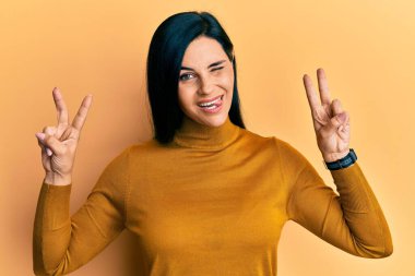 Genç beyaz kadın zafer işareti yapıyor. Kameraya seksi bir ifadeyle bakıyor. Neşeli ve mutlu bir yüzle.. 