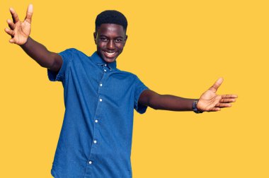 Gündelik giysiler giymiş genç Afro-Amerikan bir adam kameraya sarılıp gülümseyerek bakıyor. Mutluluğu kucaklayan neşeli bir ifade.. 